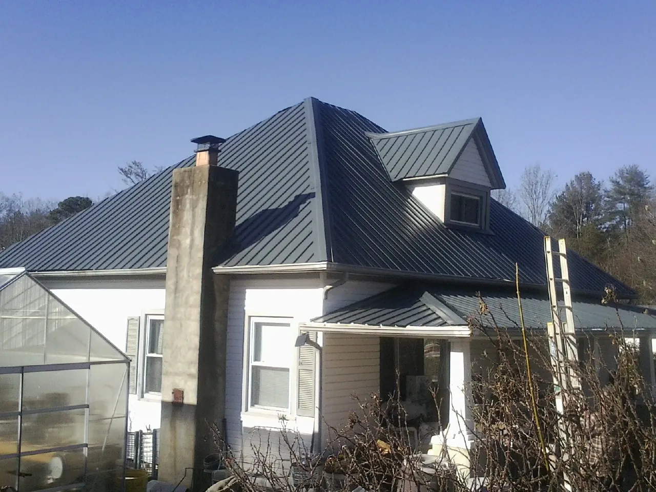 Dark blue standing seam metal roof on a white farmhouse with dormer — Slate & Tile Roof Repair by Roofing Brothers in Steamboat Rock