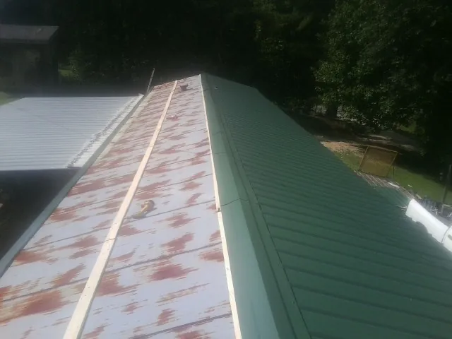Old rusted panels beside newly installed green metal roofing — Wind Damage Roof Repair by Roofing Brothers in Steamboat Rock