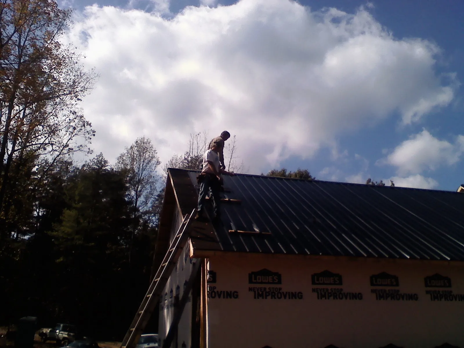 Roofer fastening dark metal panels high against a cloudy sky, from a Roof Inspection job in Steamboat Rock
