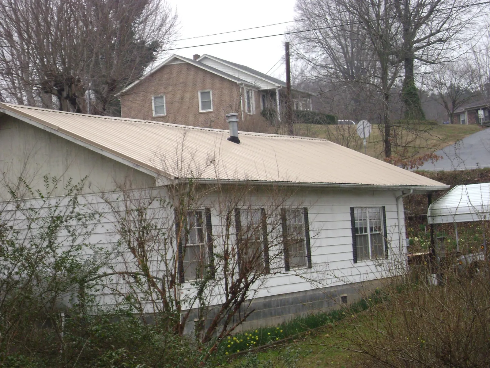 Tan metal roof on a white sided house set into a hillside — Commercial Roofing by Roofing Brothers in Steamboat Rock