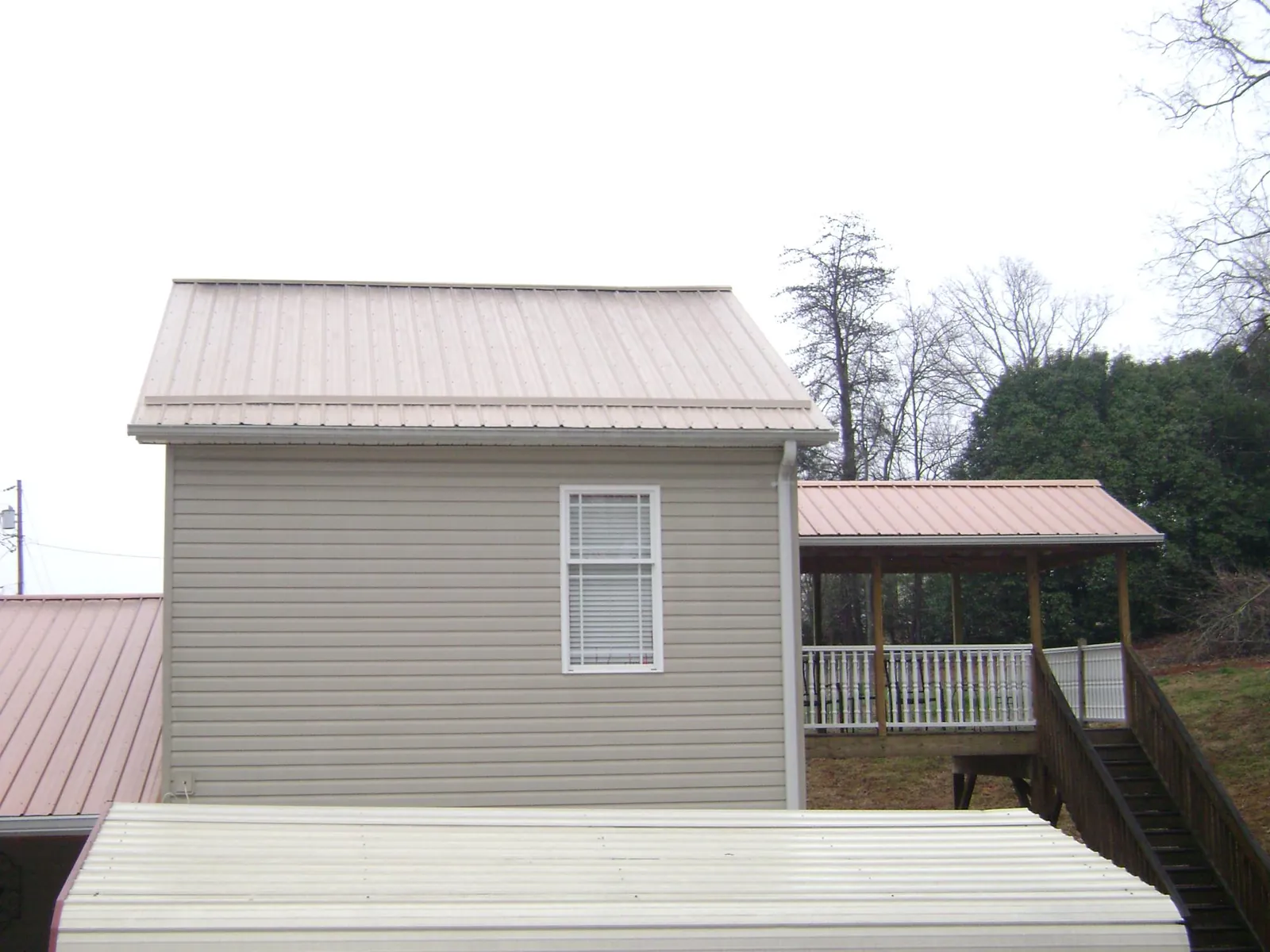 Tan metal roofs on a two story addition and attached porch, from a Roof Replacement job in Steamboat Rock