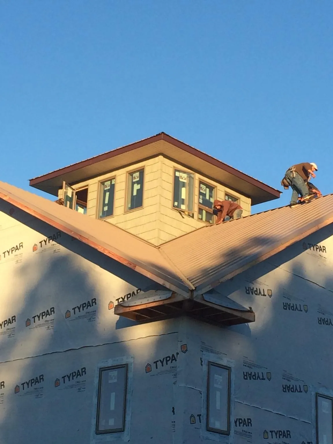 Roofers working around a rooftop cupola on a new metal roof at sunset — Roof Waterproofing in Steamboat Rock by Roofing Brothers